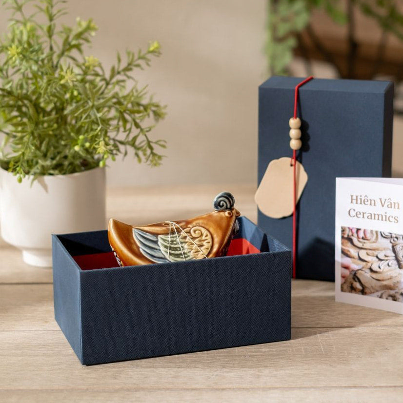 An artisan chicken statue for shelf from Hien Van pottery, sitting inside its blue gift box.