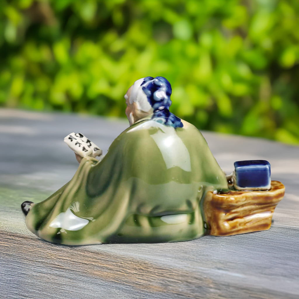 Back view of a Chinese mudmen figurine reading a scroll, on a wooden surface, perfect for bonsai figurines.