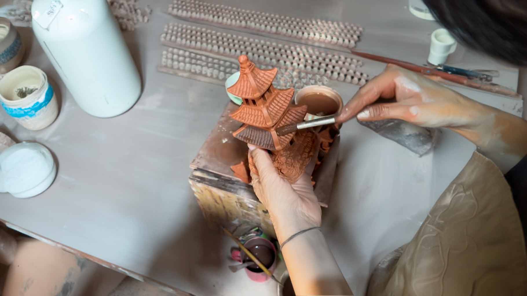 An artisan's steady hand applies delicate strokes of paint to a miniature ceramic pagoda, bringing this intricate Vietnamese ceramic statue to life at Duc Huy Pottery Workshop.