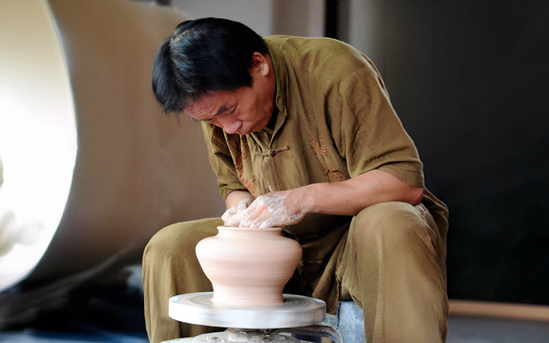 A Bat Trang ceramic artisan, with focused eyes and gentle hands, molds a clay pot on a spinning wheel, his craft a testament to generations of Vietnamese artistry.