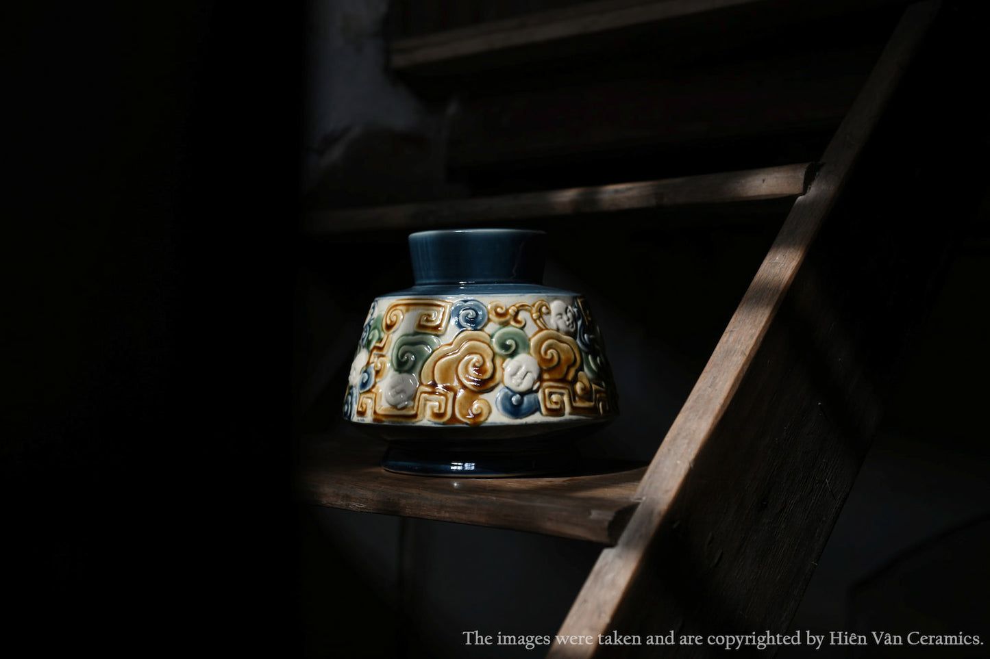 This blue Vietnamese ceramic vase with a raised cloud motif sits on a dark wooden shelf.