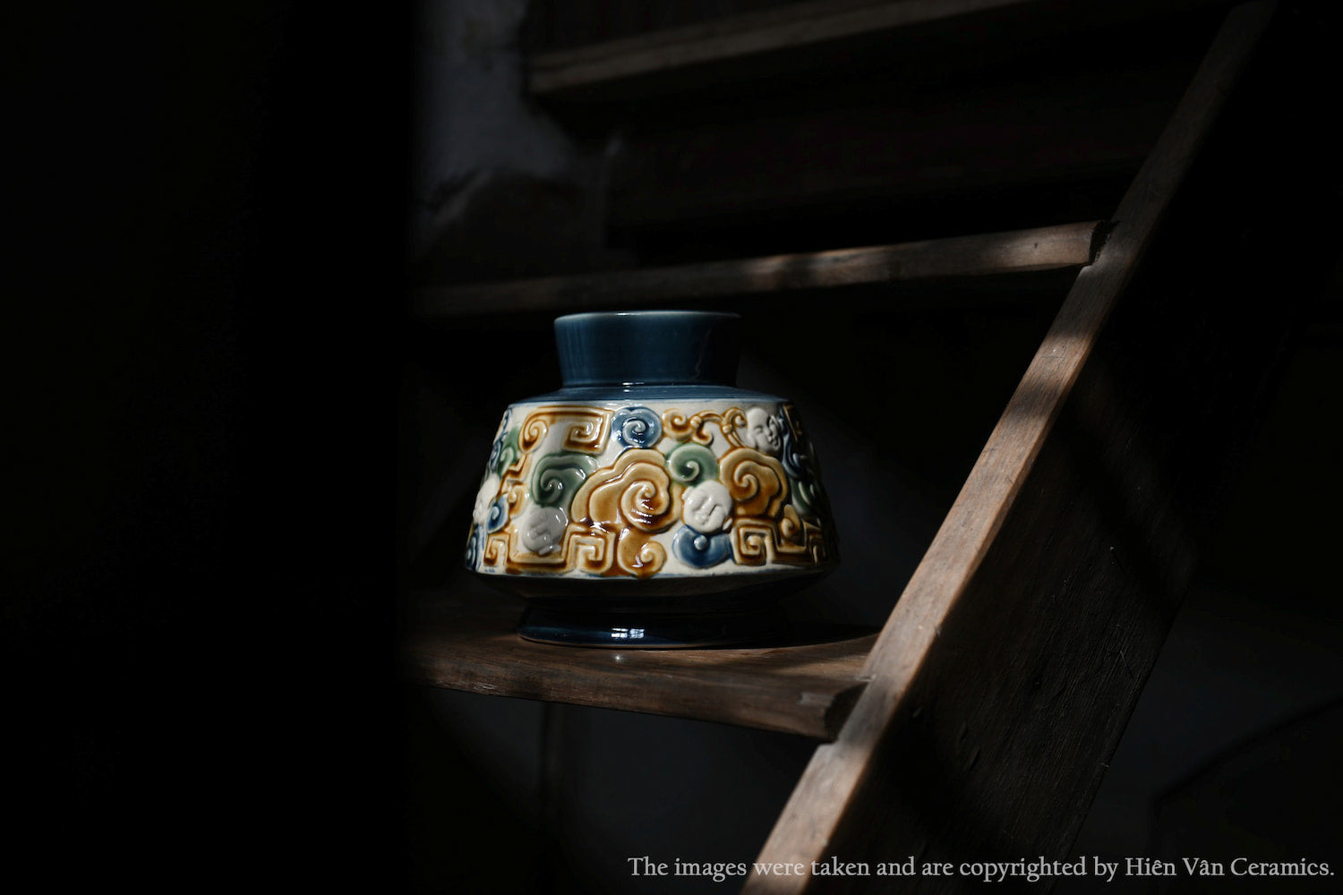 This blue Vietnamese ceramic vase with a raised cloud motif sits on a dark wooden shelf.