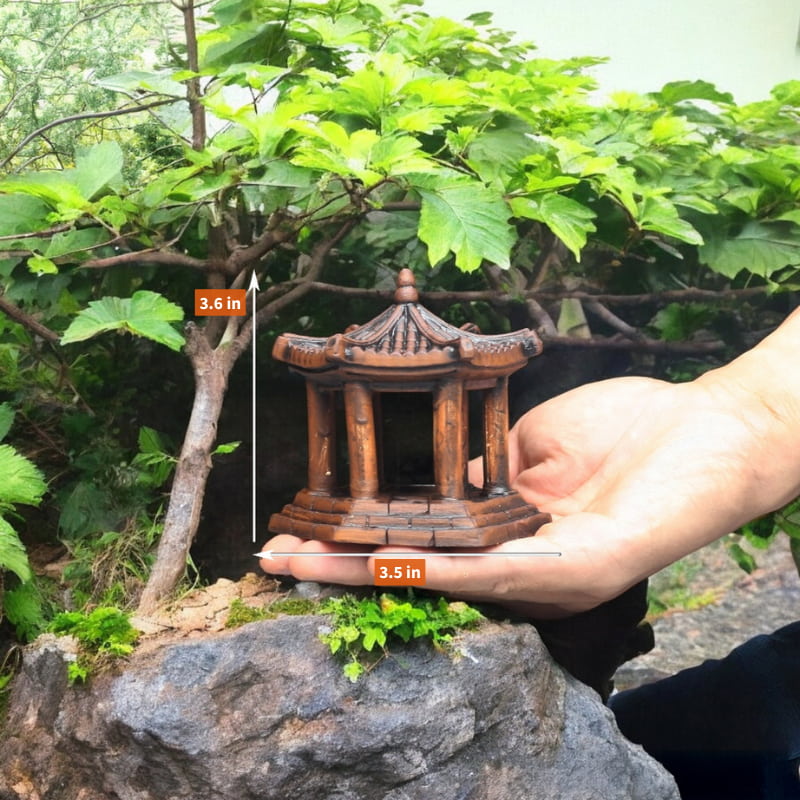 A small brown ceramic pavilion held in a hand next to a bonsai tree.