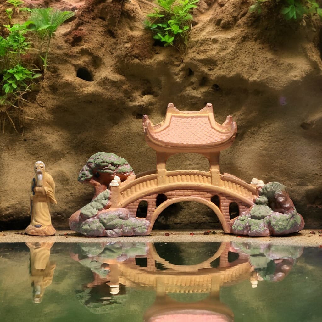 Ceramic pavilion Bonsai Bridge reflects in water, old man figurine. Garden mini bridge decor.