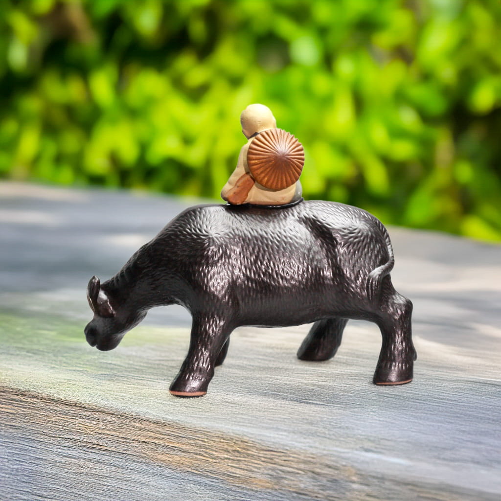 Side view: boy with round hat on black buffalo figurine. Ideal Buffalo statue Outdoor accent.