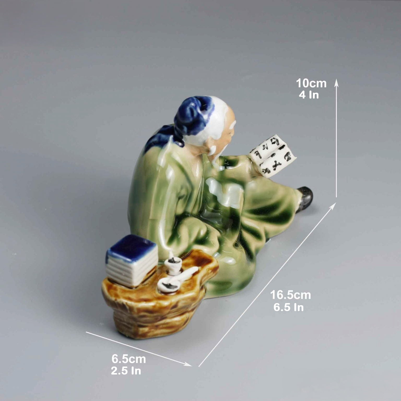 A ceramic mudman reading figurine with dimensions (10cm H, 16.5cm L), ideal for bonsai figurines decor.