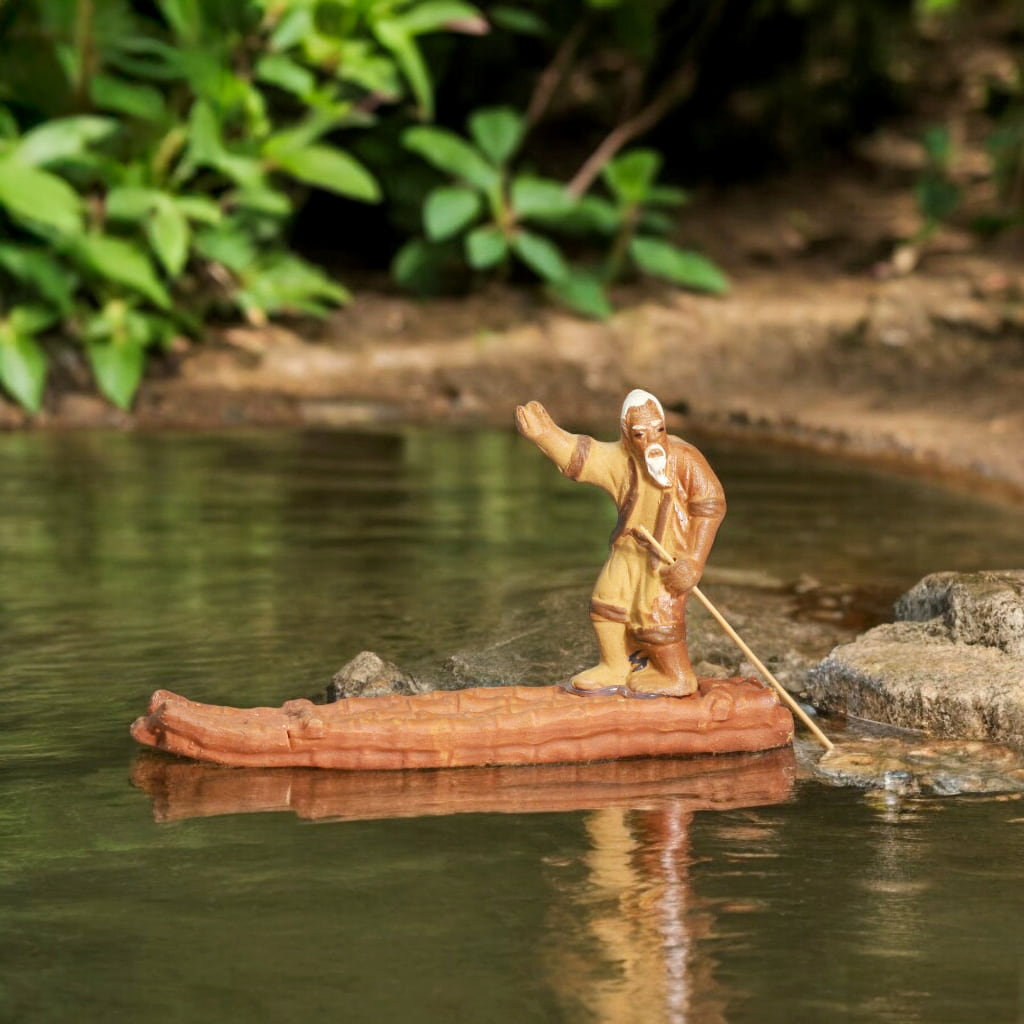 A figurine of a fisherman on a raft floating in water, capturing a serene moment of fishing.