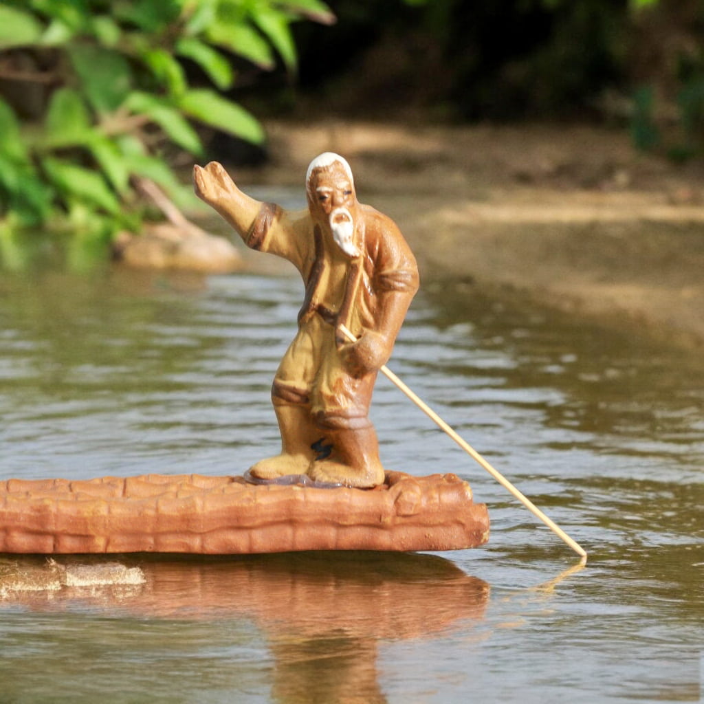 Statue of a fisherman on a raft, positioned in calm water, capturing a serene moment of maritime life.