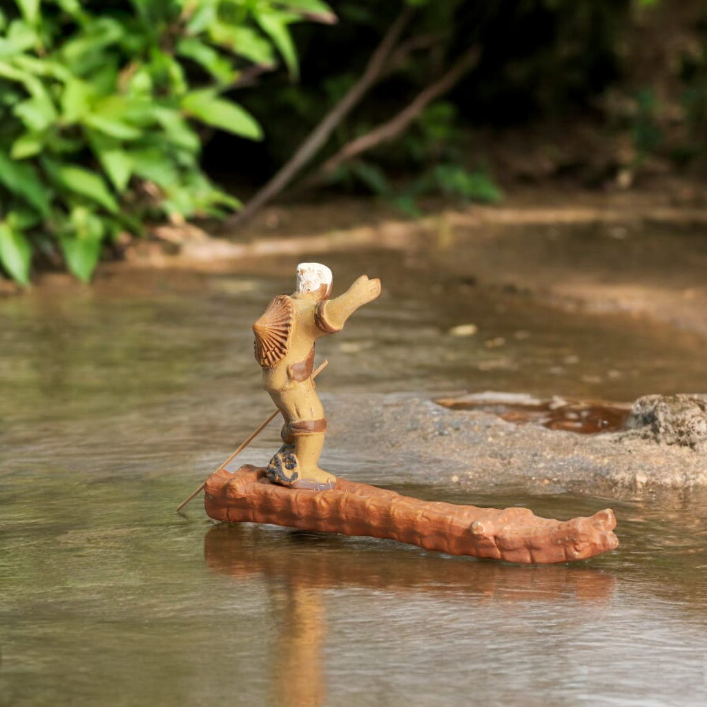 Fisherman figurine sitting on a raft in the water, capturing a serene moment of outdoor leisure.