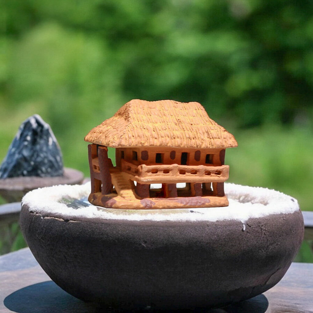 Side view of mini house figurines, a brown stilt house with stairs, in a bonsai pot.