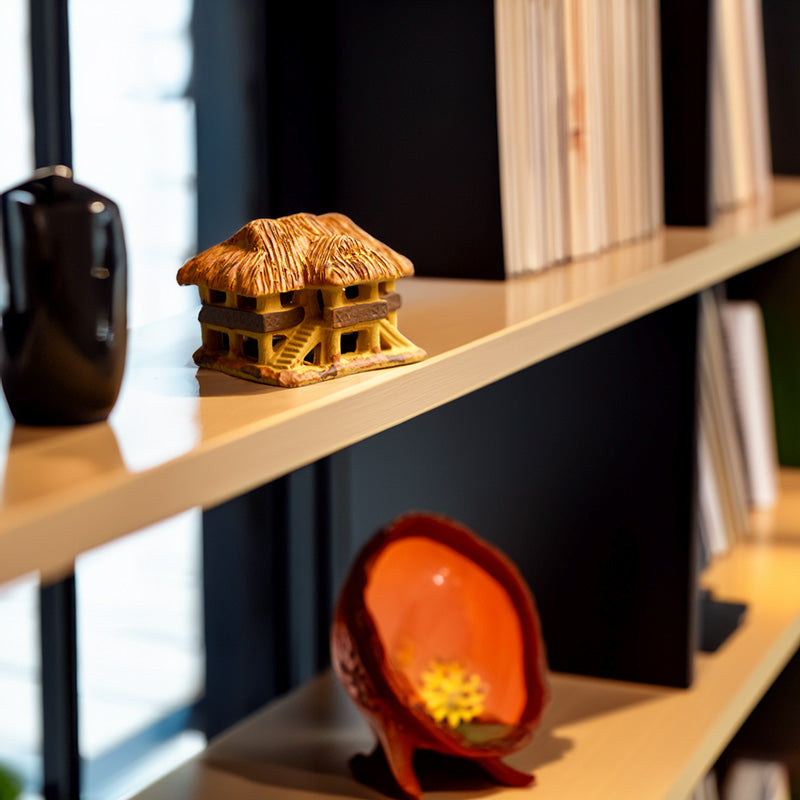This handcrafted miniature Vietnamese stilt house, perched on a modern bookshelf, adds a touch of cultural charm and warmth to any home décor.