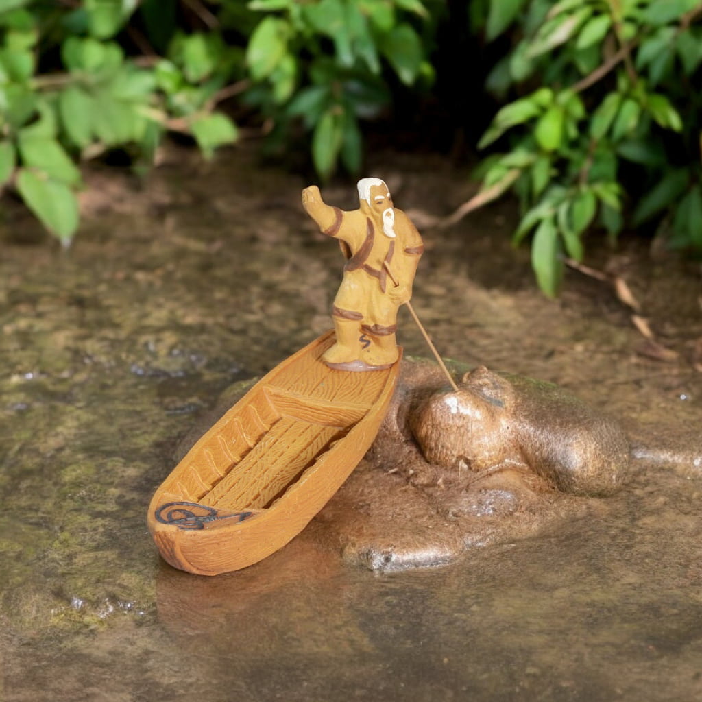 A ceramic figurine of an old fisherman rowing a wooden boat.