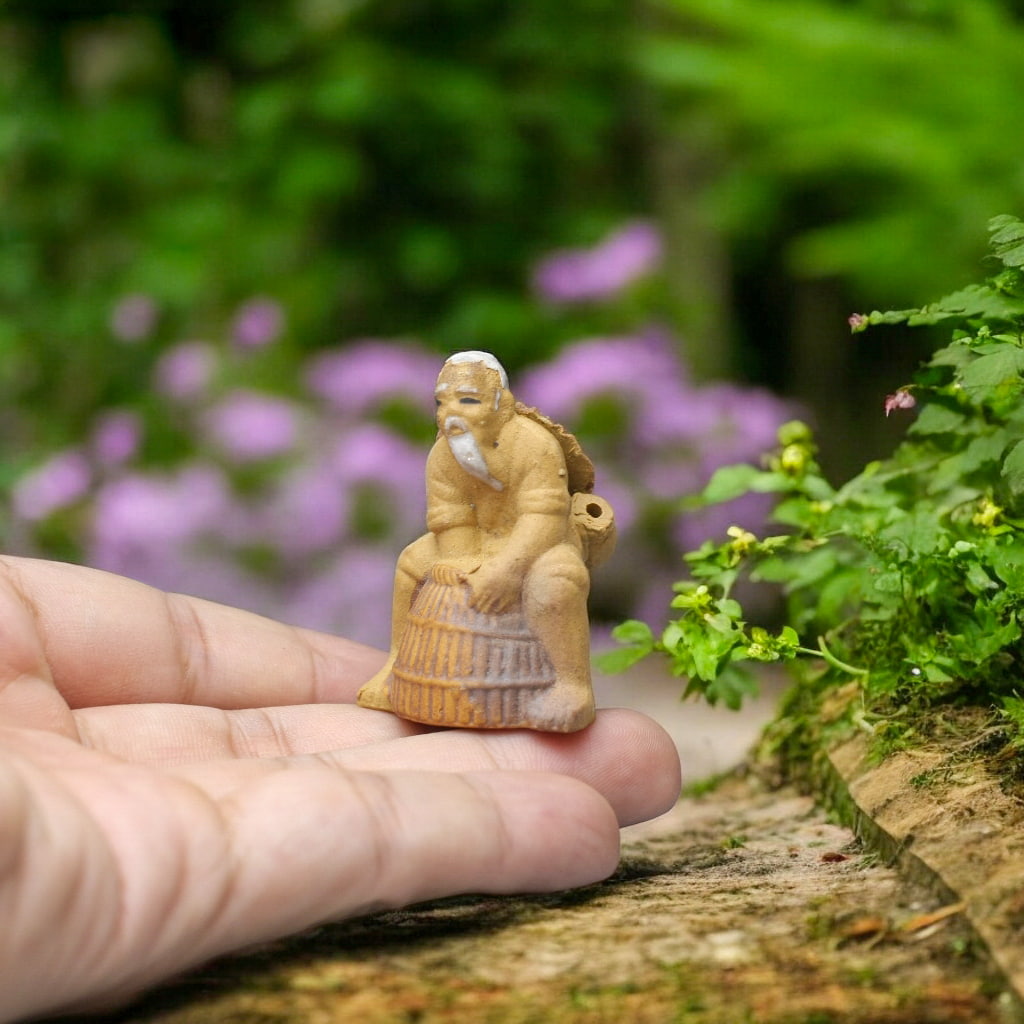 A chinese mudman fisherman sits on a barrel on a hand. Unique ceramic aquarium ornaments.