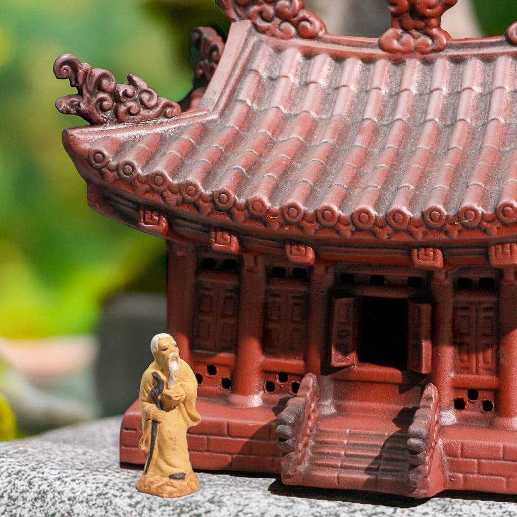 Tiny robed bonsai figurine by reddish-brown pagoda statue steps. Handcrafted pagoda statue detail.