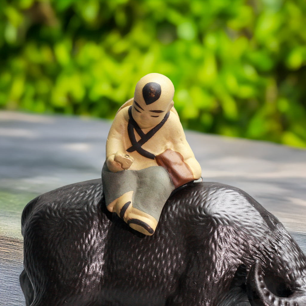 Close-up: serene boy sits on textured black buffalo sculpture. Unique buffalo figurine.