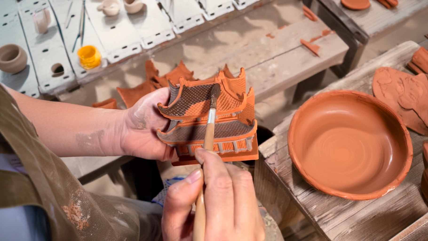 In the heart of Bat Trang village, a skilled artisan meticulously hand-paints a miniature ceramic pagoda, showcasing the dedication and artistry behind each Vietnamese ceramic statue.