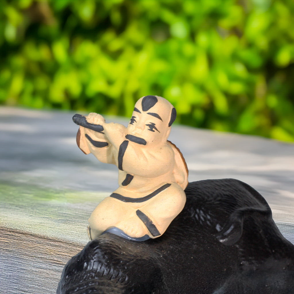 Boy playing flute on a buffalo statue. Detail of the buffalo figurine.