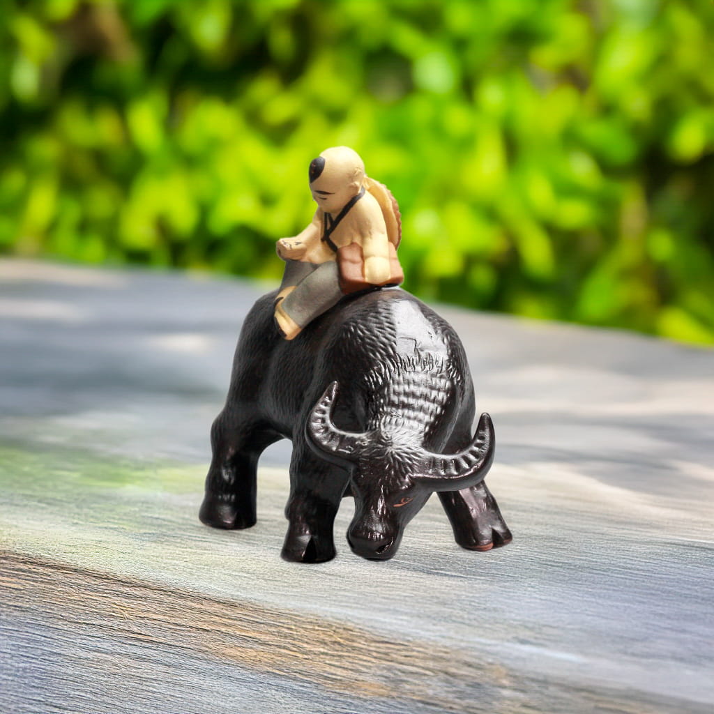 Boy in simple tunic rides a black buffalo statue. Rustic buffalo sculpture for bonsai.