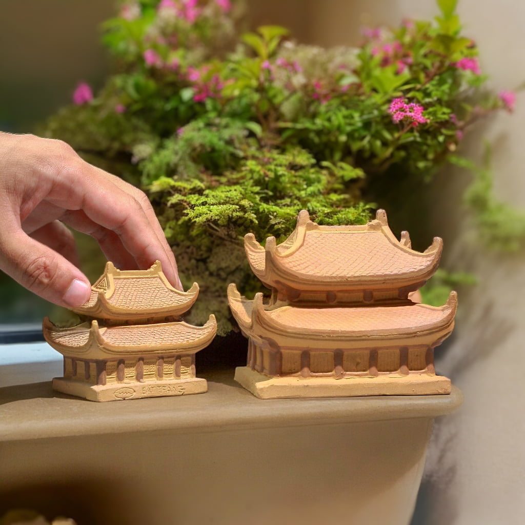 Hand holds two handcrafted pagoda statue sizes. These bonsai figurines are miniature pagodas.