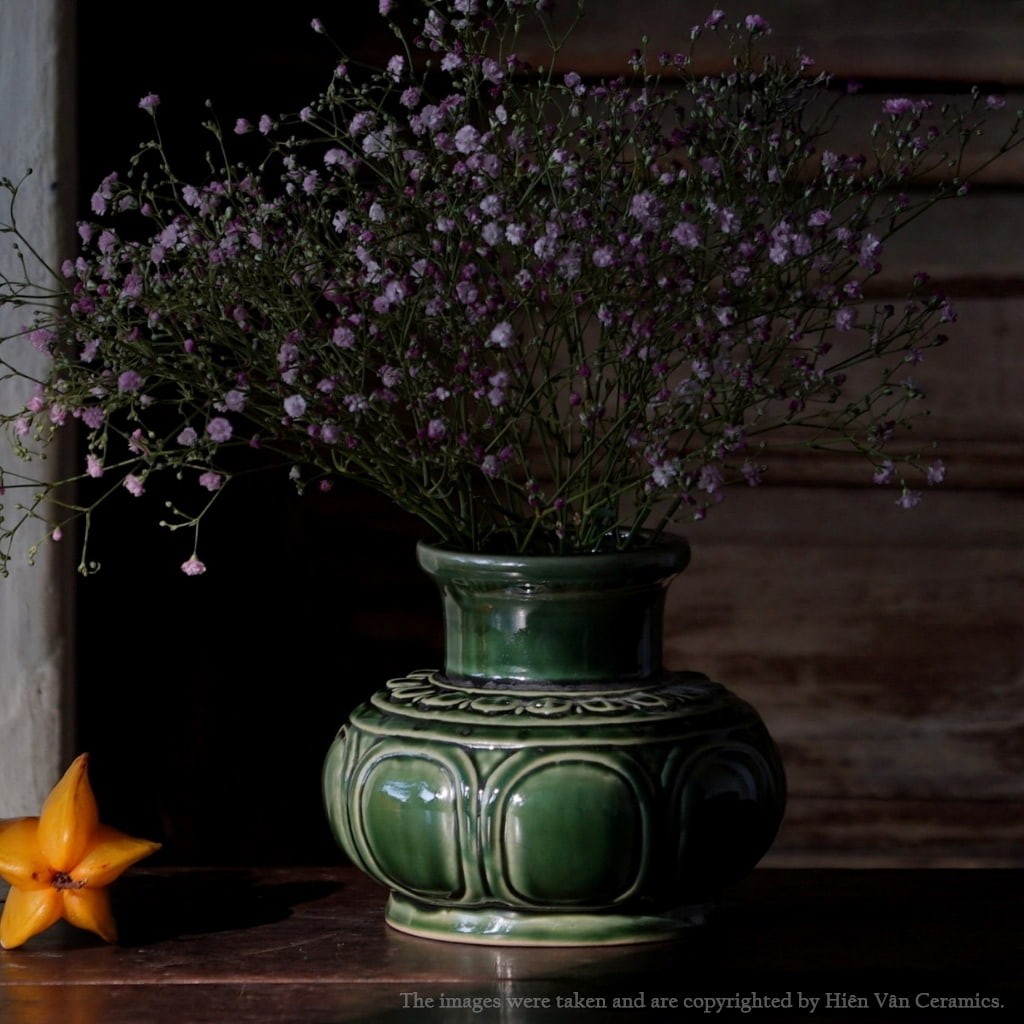 A green Vietnamese ceramic vase in low light. This low wide flower vase holds baby's breath.