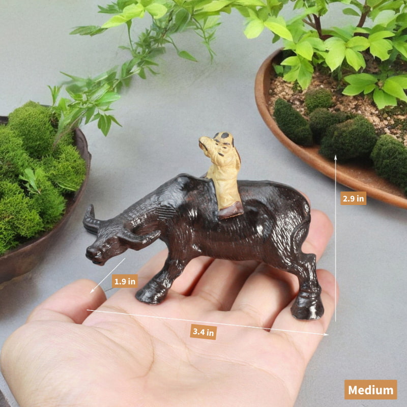 A hand is holding a medium-sized, dark brown ceramic statue of a boy riding a water buffalo.