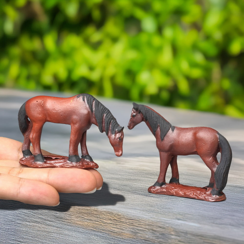 Two small, reddish-brown ceramic horses rest on a hand, showcasing their detailed craftsmanship.