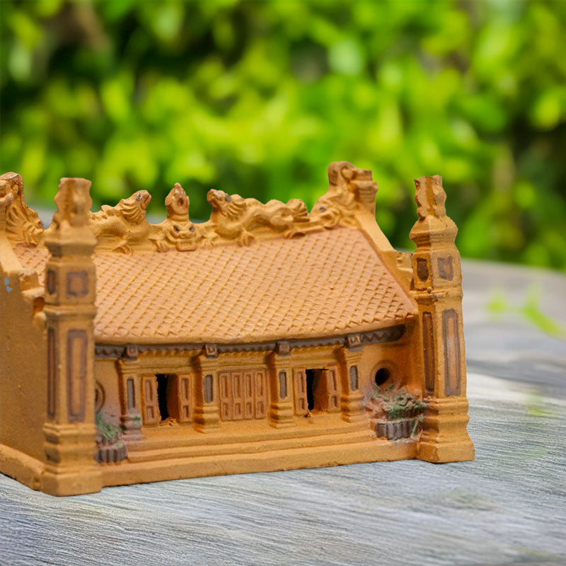 A rustic brown ceramic miniature temple, meticulously crafted with traditional Vietnamese architecture, sits peacefully on a wooden surface, adding a touch of serenity to any miniature landscape.