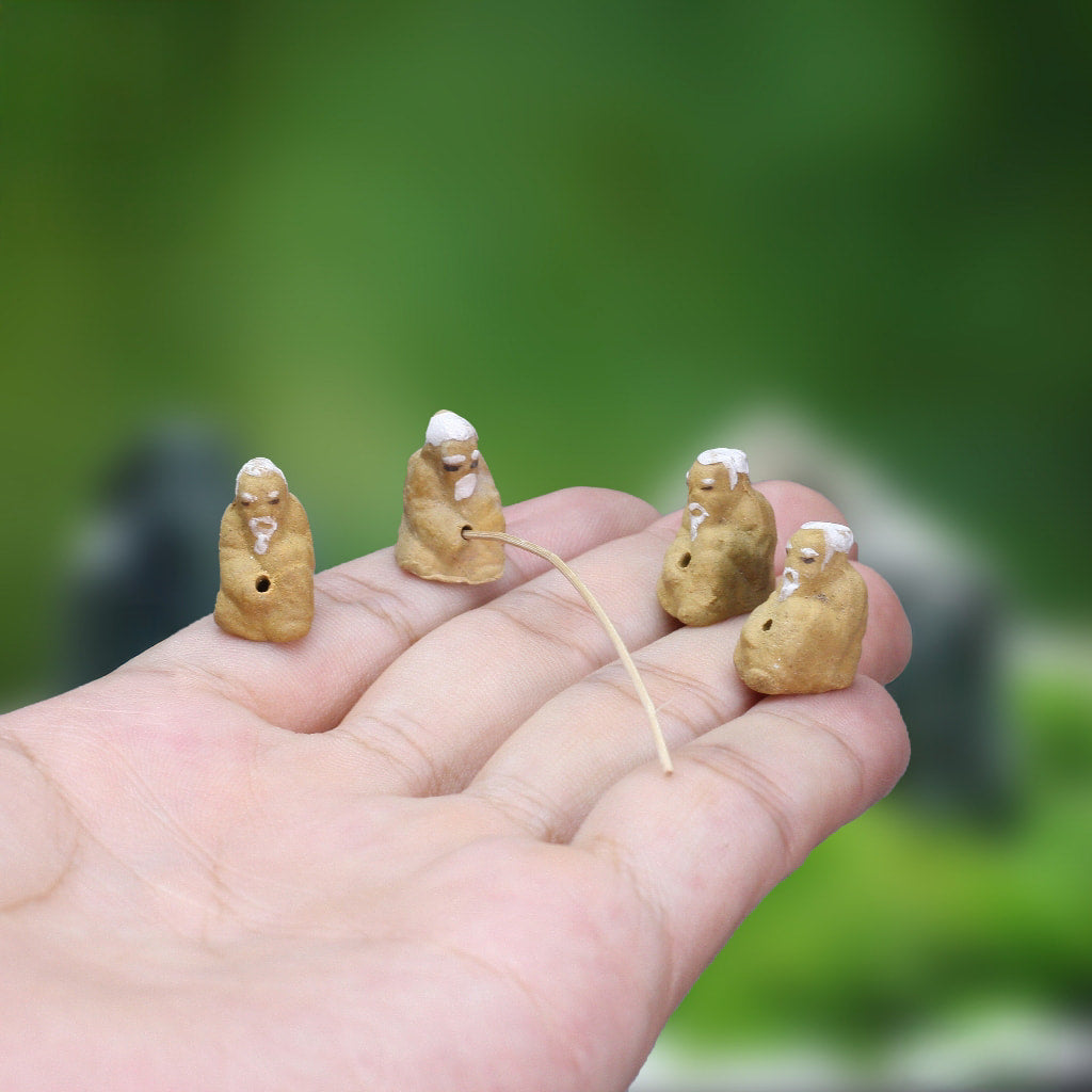 Miniature ceramic figurines of four fishermen sitting on a hand, showcasing intricate details of traditional mudmen craftsmanship.