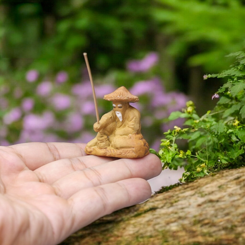 Small fishing figurine with hat, holding rod, on a hand. Classic chinese mudman fisherman style.