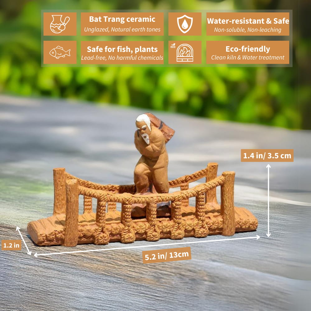 A small ceramic bridge with a rope railing, sitting on a wooden surface. A small figure of an old man is walking across the bridge. The bridge is unglazed and has a natural brown color.
