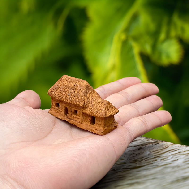 A miniature Vietnamese thatched cottage, crafted from rustic terracotta clay, rests delicately in a hand, showcasing its intricate details and charming simplicity
