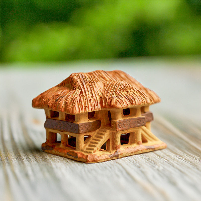 A charming miniature Vietnamese stilt house, crafted from warm terracotta ceramic, stands proudly on a rustic wooden surface, its thatched roof adding a touch of authenticity.
