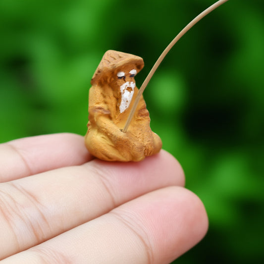 A small mudmen fisherman figurine with a rod resting in an open palm, showing texture.