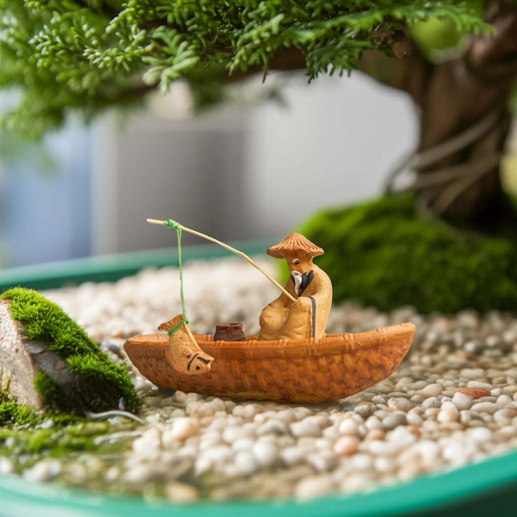 A fishing figurine in a boat sits under a bonsai tree, a unique bonsai decoration.