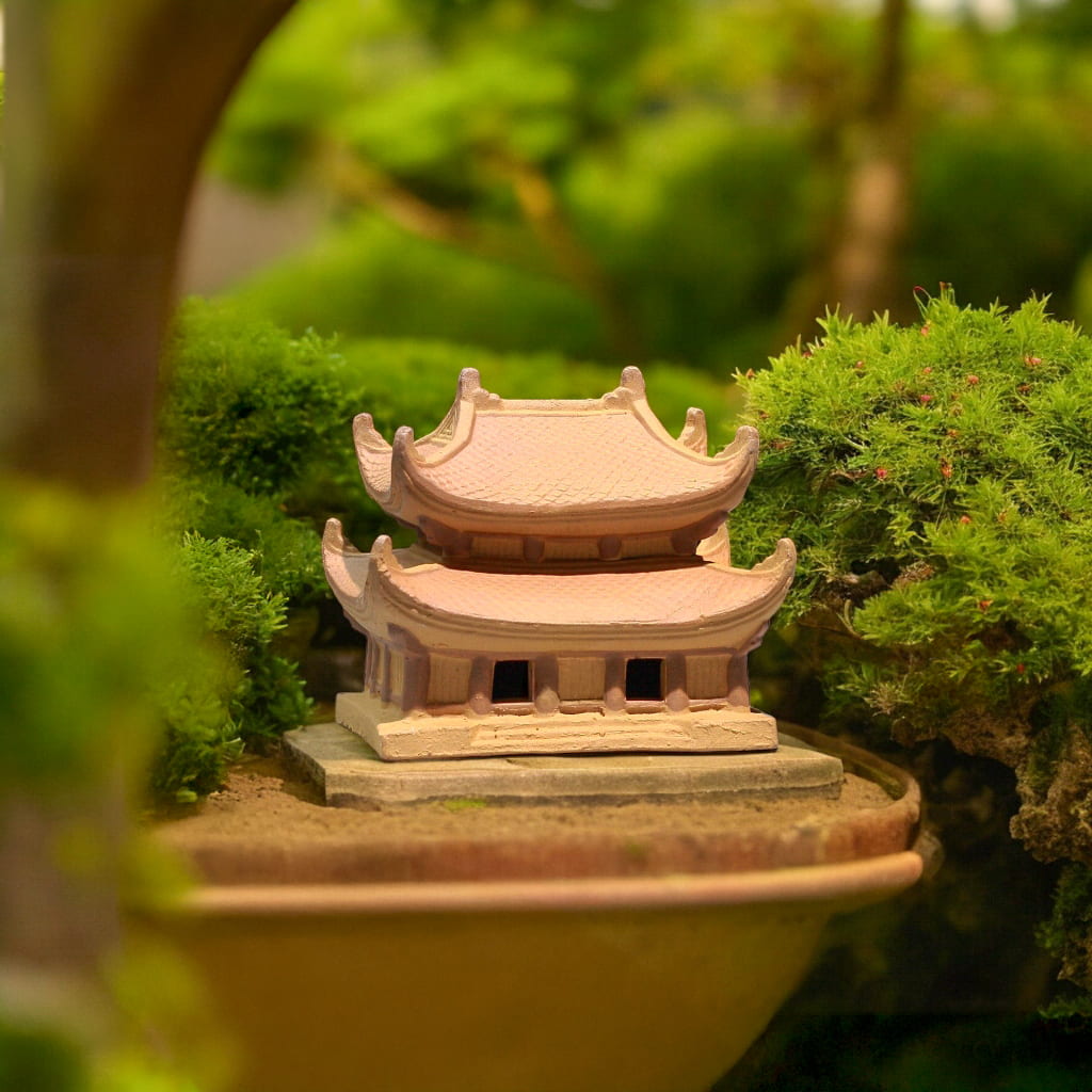 A miniature pagoda for bonsai sits in moss. Zen garden pagoda statue for bonsai decor.