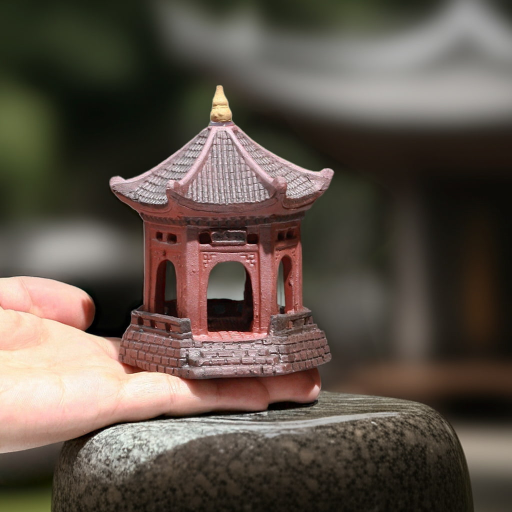 A hand holds a red-brown miniature pagoda over a stone. It's a small pagoda statue, ideal bonsai figurines.