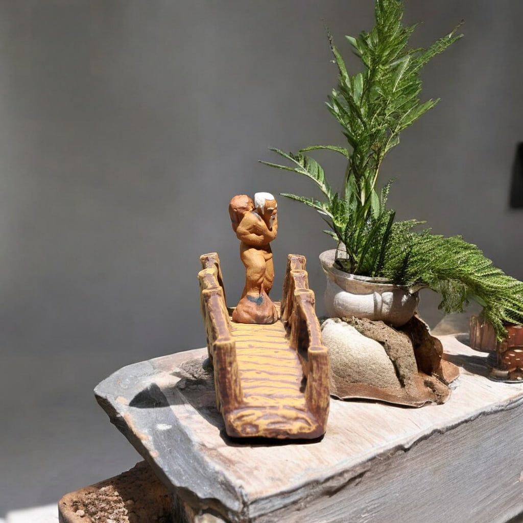 Brown ceramic miniature bridge with yellow path, a Bonsai Bridge near a plant.