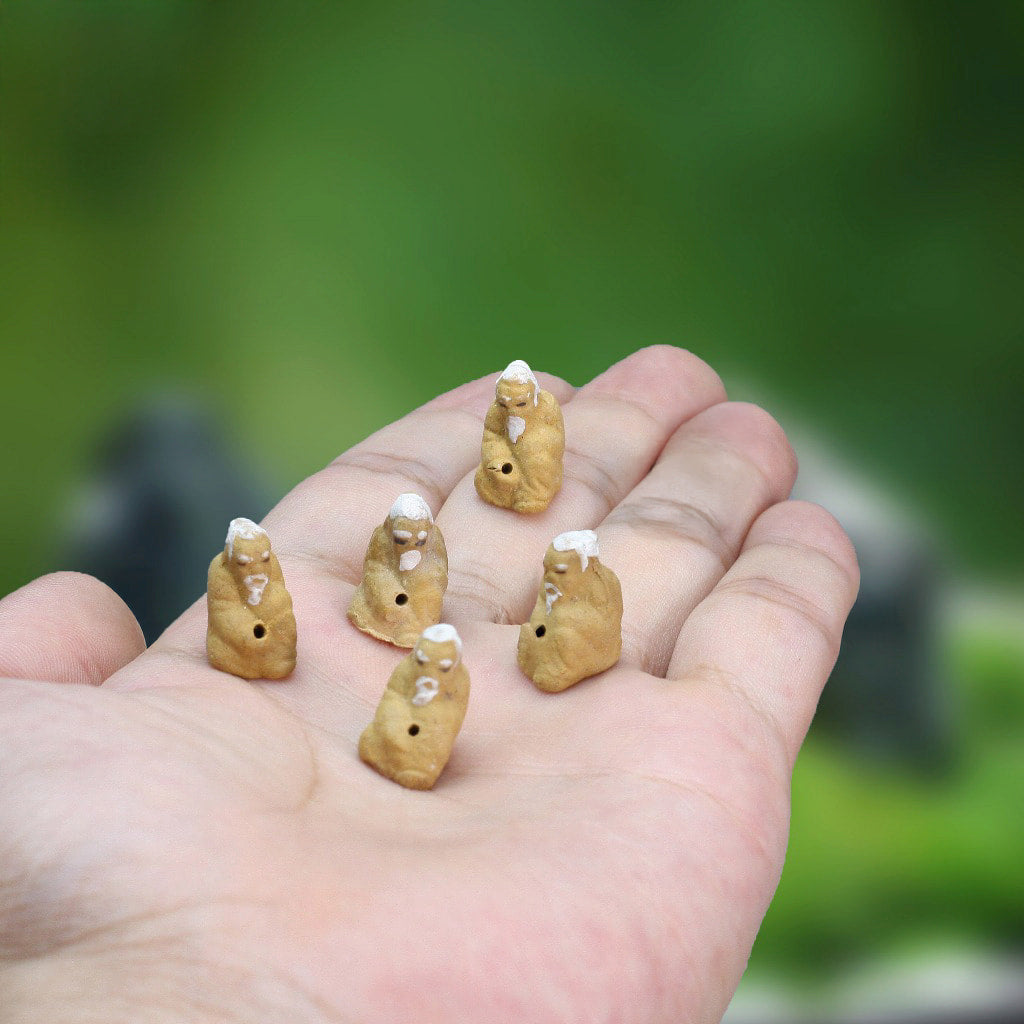 A person holds miniature figurines of bonsai fisherman.