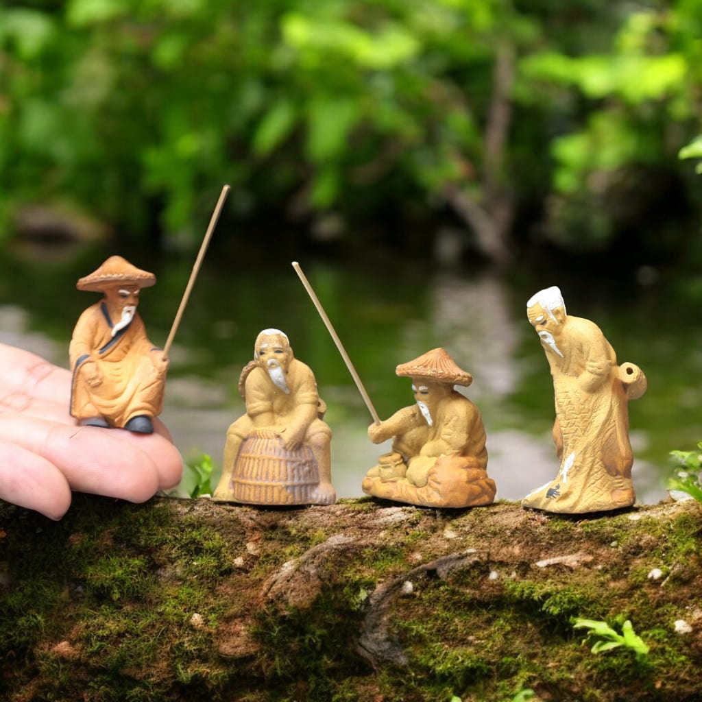 Four small, tan fisherman ceramic figurines. One on a hand, three on mossy wood. Good for bonsai.