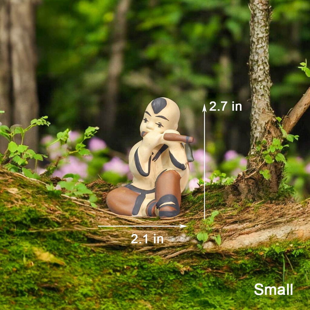 A small ceramic figurine of a boy sits on a mossy log, playing a flute. He wears a cream top and brown pants.