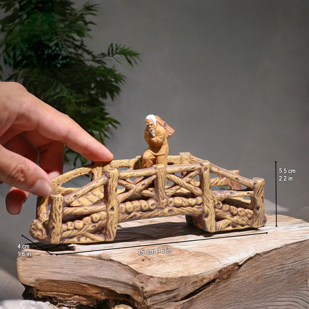 Hand holds a brown ceramic small garden bridge; a detailed miniature bridge