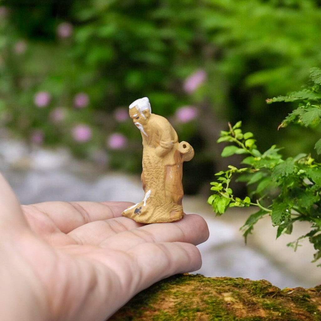 Standing fisherman ceramic figurine with basket on back, held in hand. Detailed fishing figurine.