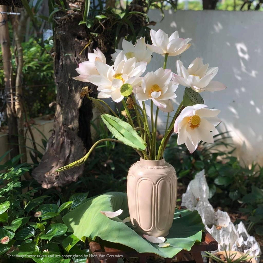 A beige ash glaze vase with white lotus. This is a tall ceramic vase for flowers in a garden.
