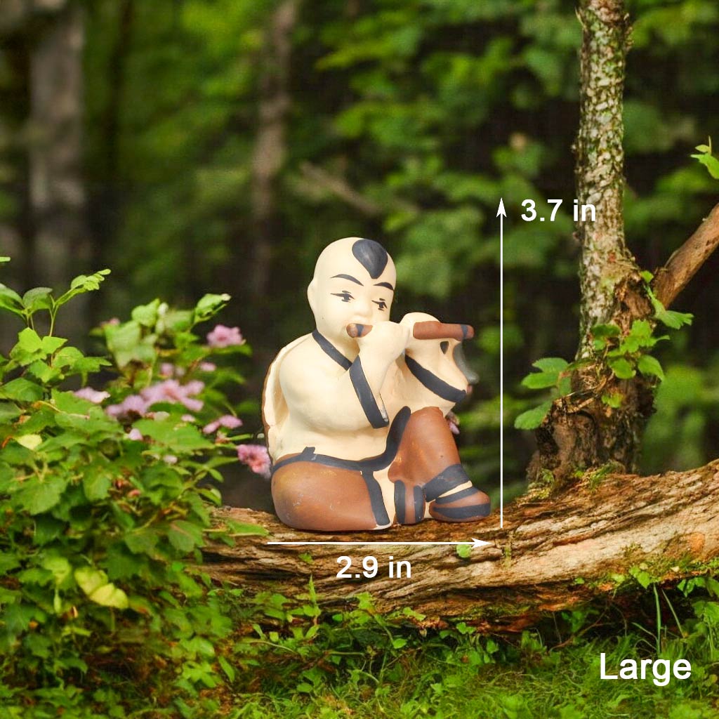 A ceramic figurine of a boy sits on a mossy log, playing a flute. He wears a cream-colored top and brown pants.
