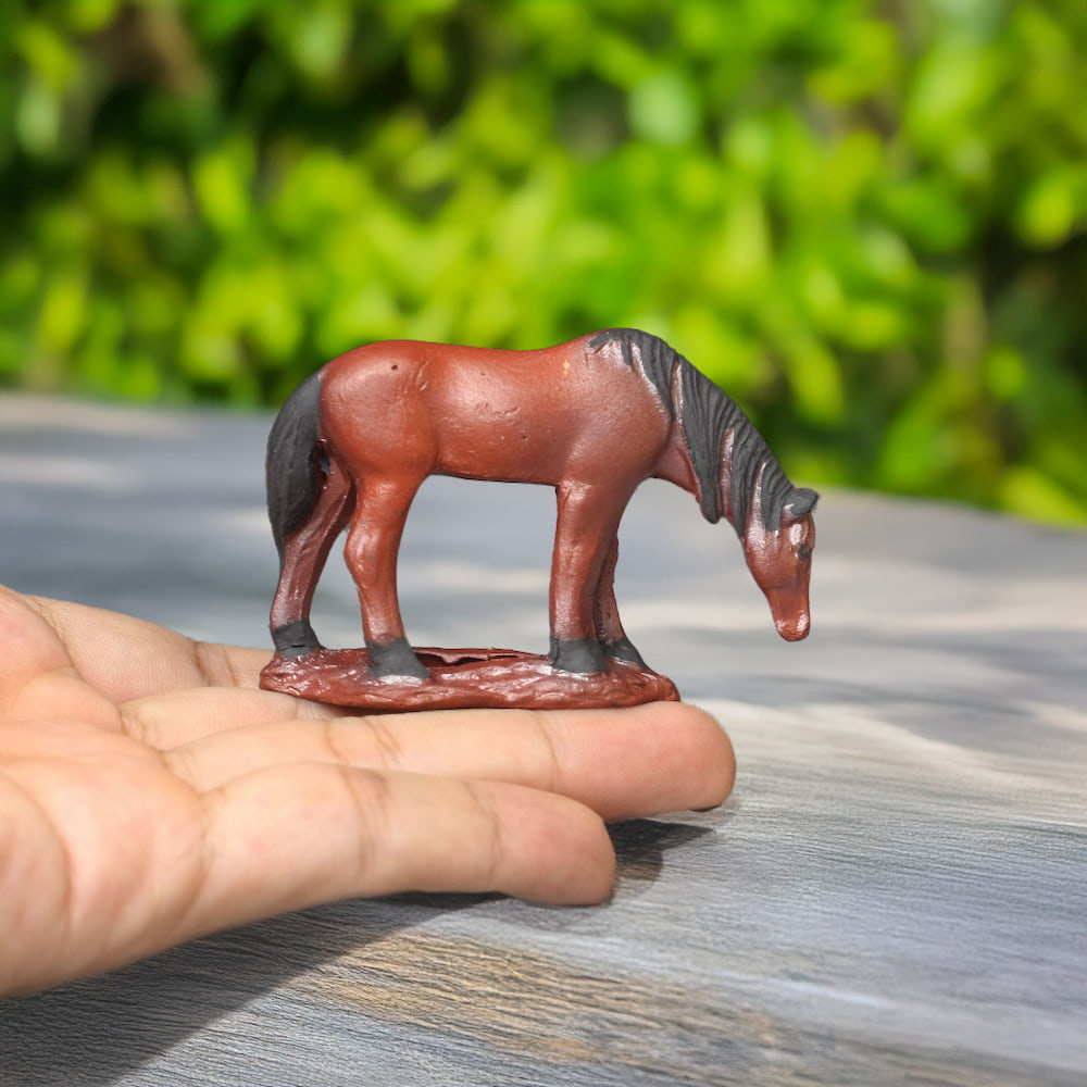 A tiny, brown ceramic horse with a dark mane, head bowed, is held gently in a hand.