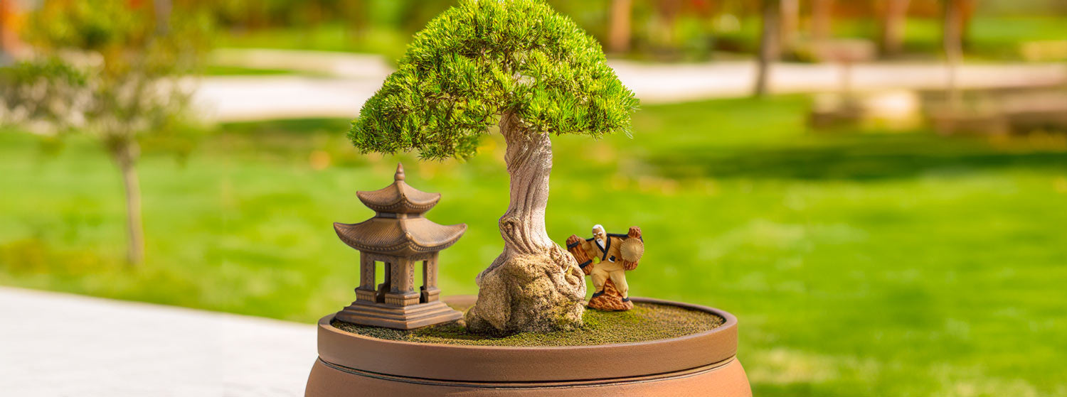 Under the shade of a bonsai tree, a miniature ceramic pagoda stands tall, its intricate details echoing traditional Vietnamese architecture, while a whimsical mudman figurine adds a touch of charm to this miniature landscape.