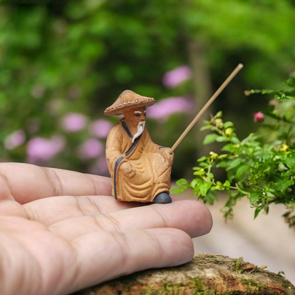 Tiny fisherman statue in yellow robe, holding rod, on a hand. Great ceramic aquarium decor.