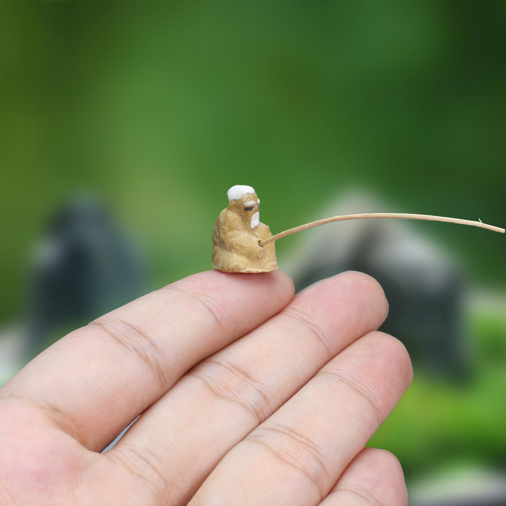 A miniature ceramic mudmen fisherman figurine perched on a person's hand
