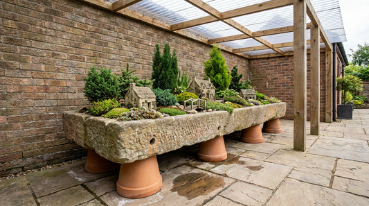 A wide miniature garden planter raised on feet in a sheltered outdoor corner.