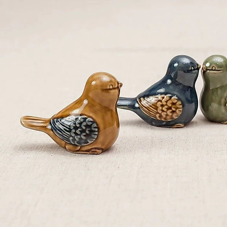 Three Vietnamese ceramic bird figurines in yellow, blue and green lined up in a row